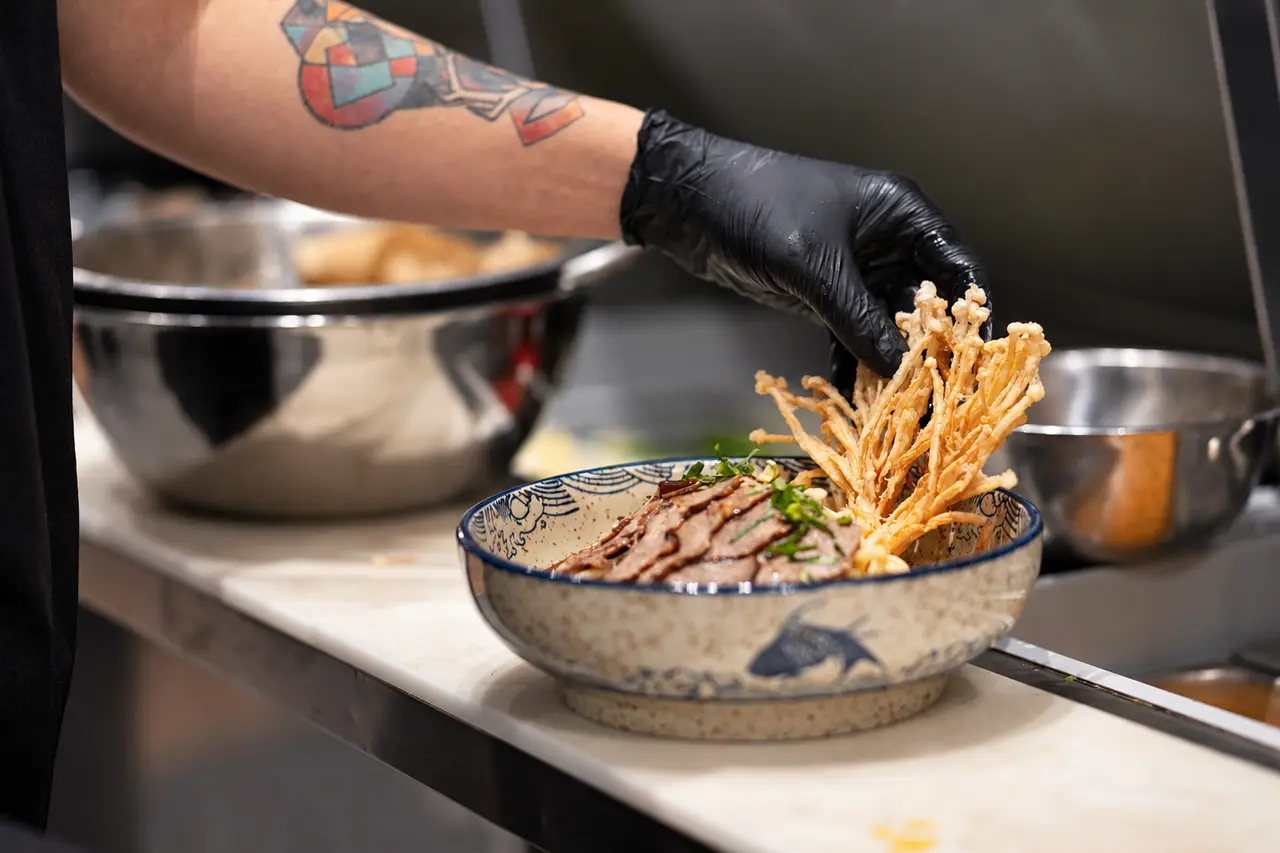 A gloved cook finishes a bowl with crispy enoki in the RUAM kitchen.